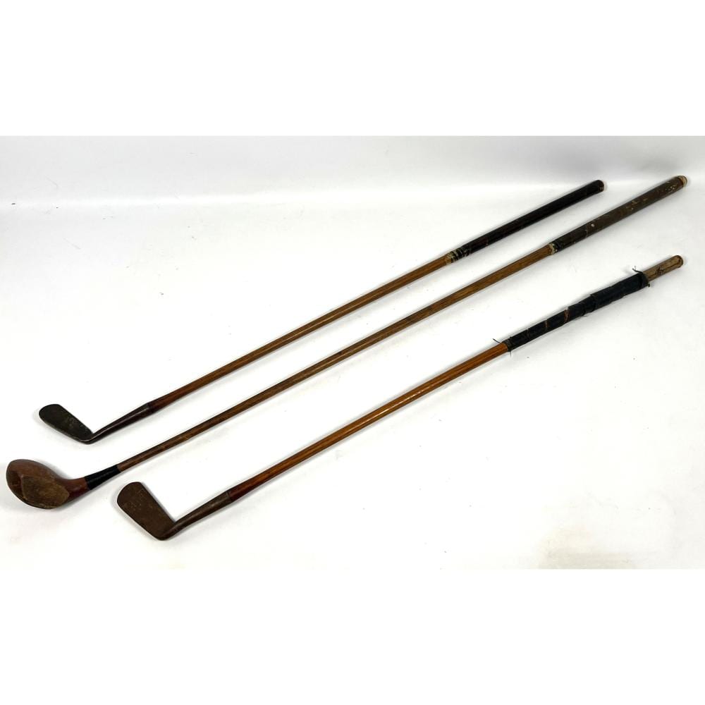 Three vintage golf clubs with wooden shafts and dark club heads arranged on a white background.
