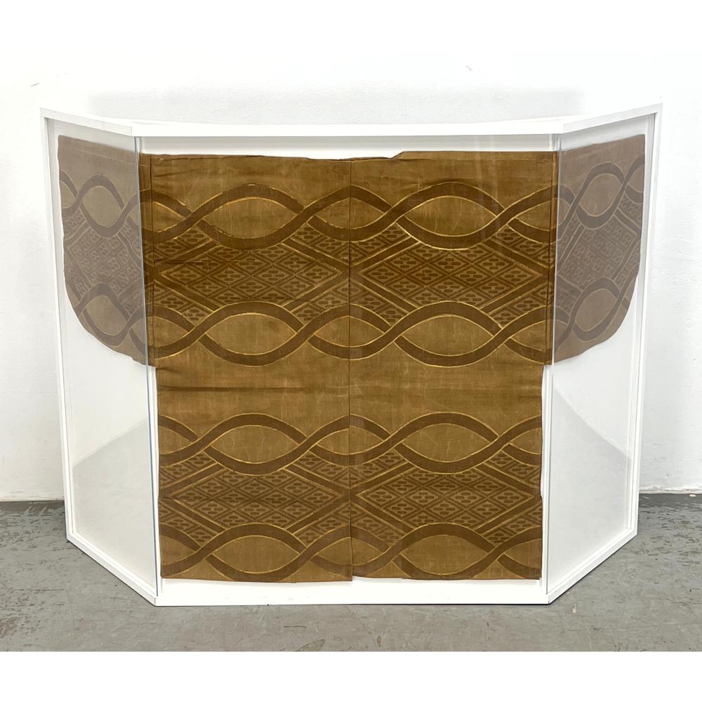 Front view of a folded brown textile with repeating wave and diamond motifs displayed inside a white frame