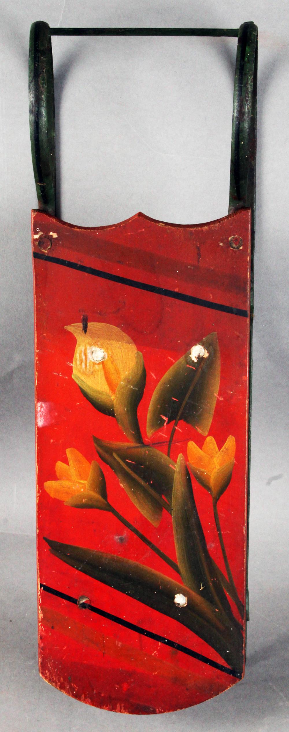 Antique red toy sled with dark green runners and painted floral and leaf design on the front panel.
