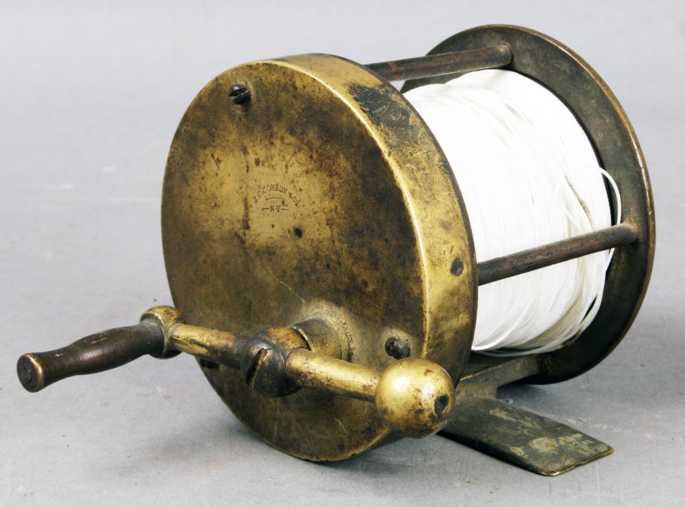 Antique brass baitcasting fishing reel with a spool of white line, shown at an angle with a metal handle and winder.