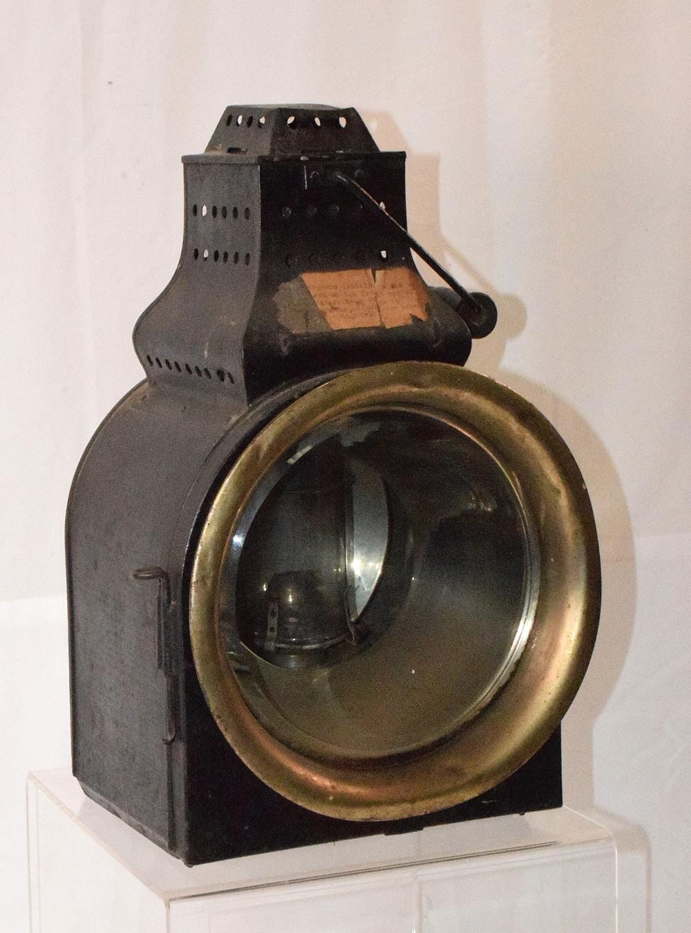Antique railroad lantern with a glass lens and metal housing, black body with a brass-colored rim.
