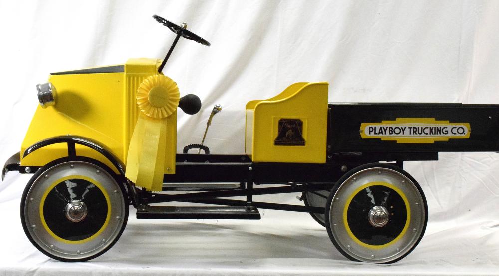 Yellow and black pedal truck with large wheels and a side panel reading “PLAYBOY TRUCKING CO.”