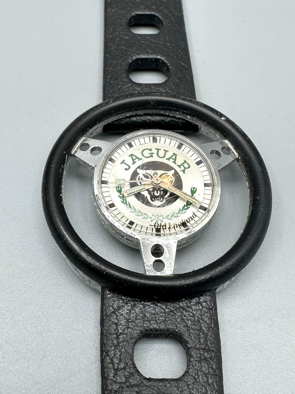 Close-up of a vintage-style wristwatch face showing “JAGUAR” and a leaping animal emblem, with a black leather strap.