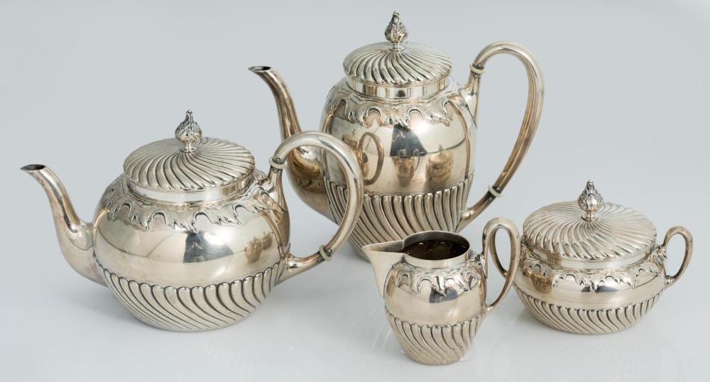 Four-piece polished silver-toned coffee and tea set with teapots and sugar creamer, featuring ribbed sides and dome lids with finials.