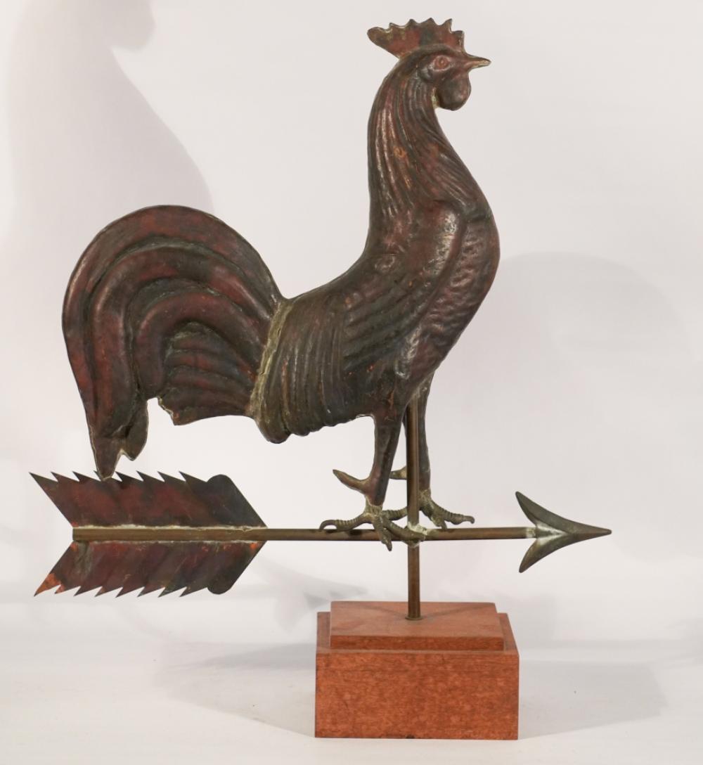 Antique copper rooster weathervane with a winged tail and arrow-like direction fin, mounted on a metal post.