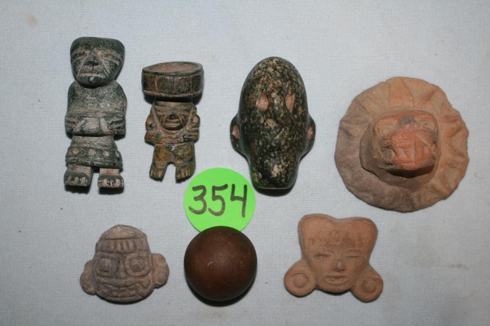 Photograph showing seven small carved artifacts arranged on a light background, including two seated figurines and several heads and beads.