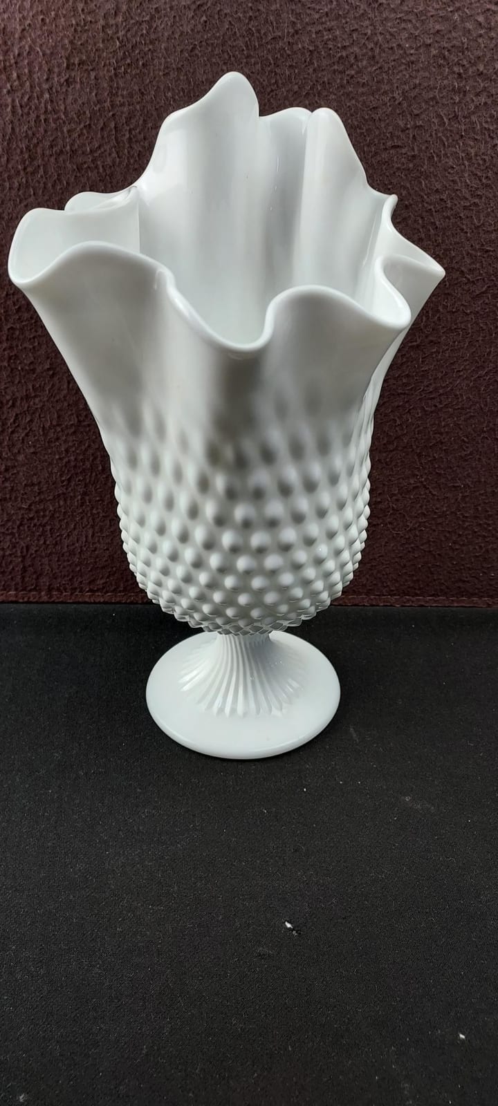 White milk glass hobnail vase with raised bumps and a flared ruffled rim, resting on a black surface.