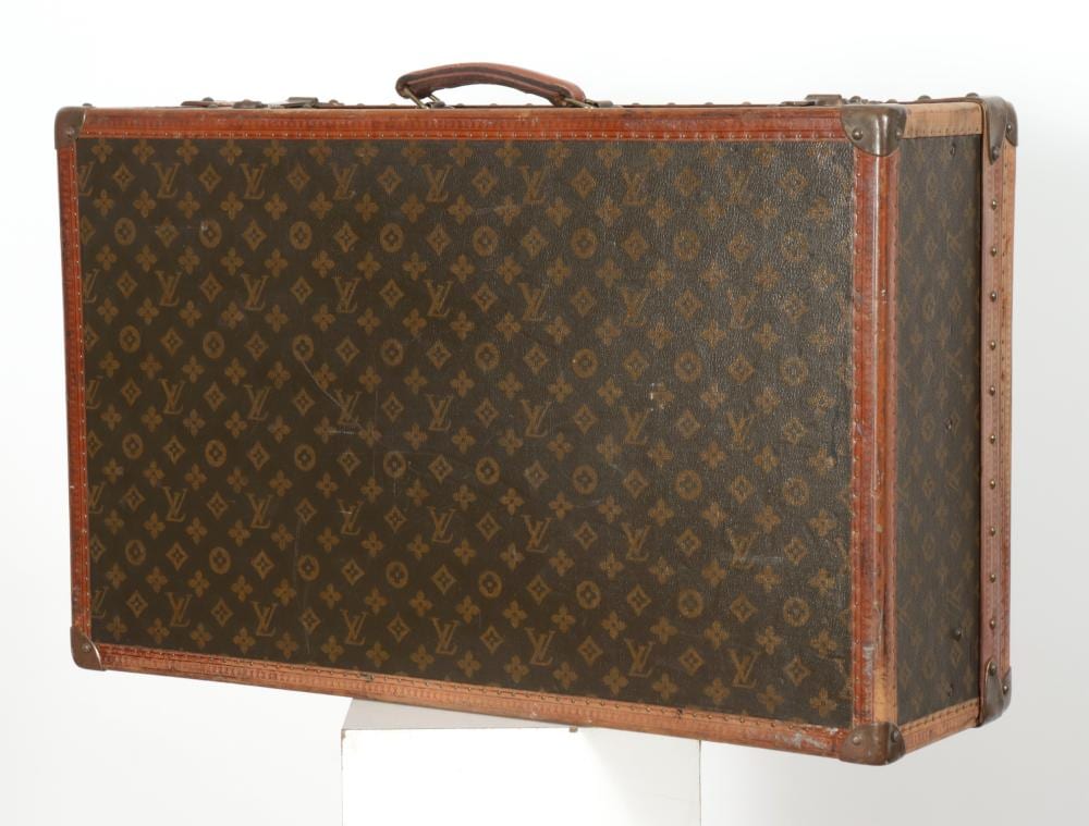 Brown vintage suitcase with a monogram pattern, leather trim, and metal corner hardware, shown from the front.