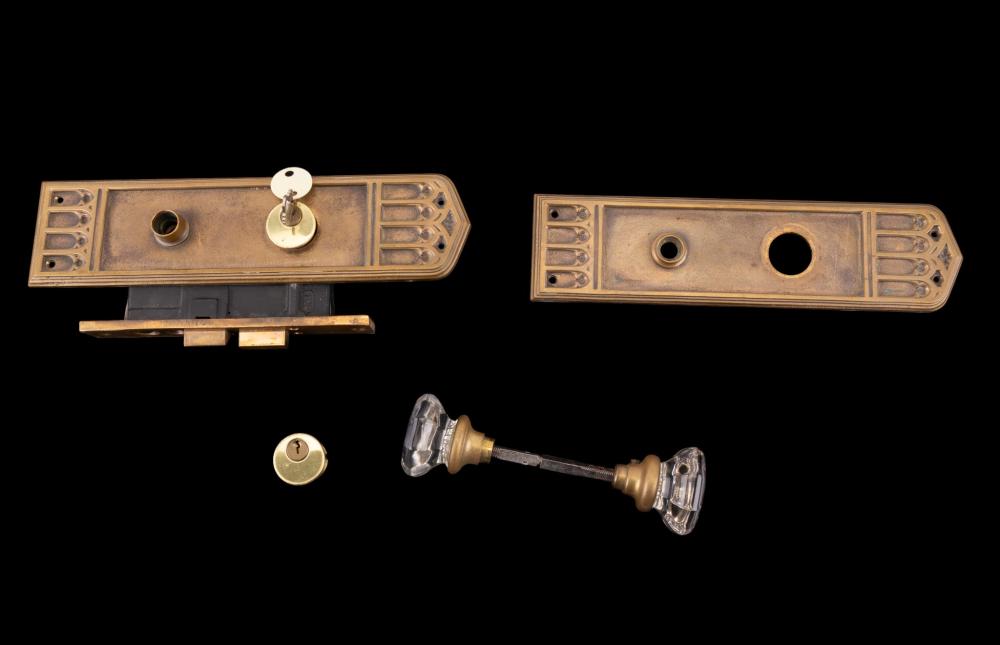 Set of antique-style bronze door hardware parts on a black background, including two rectangular plates, a knob backplate, and a clear glass knob.