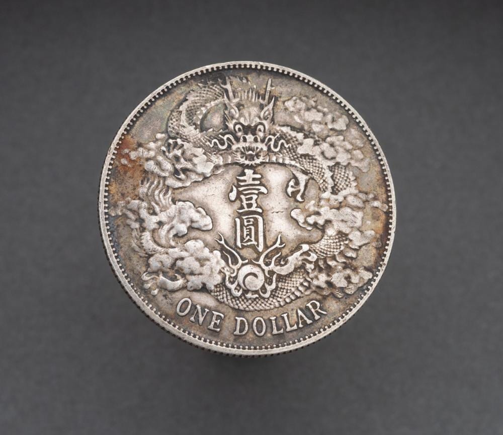 Close-up of a silver coin showing a detailed dragon, clouds, Chinese characters, and the word “ONE DOLLAR” around the edge.