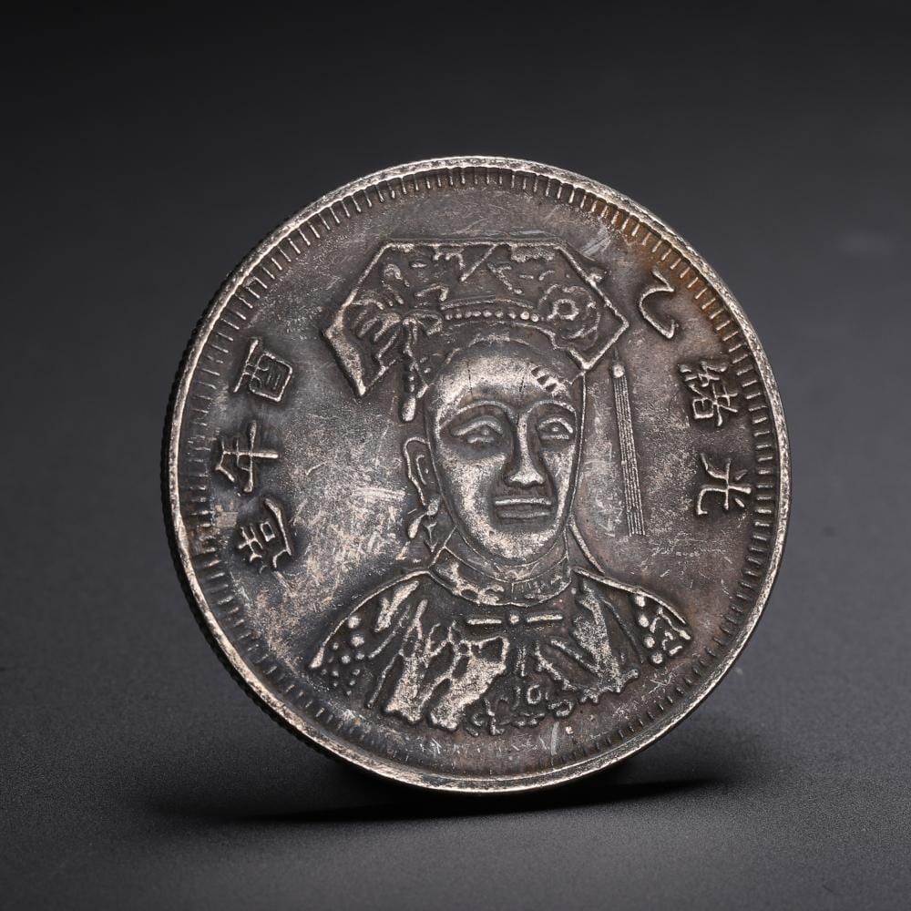 Close-up of a round Chinese-style silver coin with a face portrait in the center and Chinese characters around the rim.