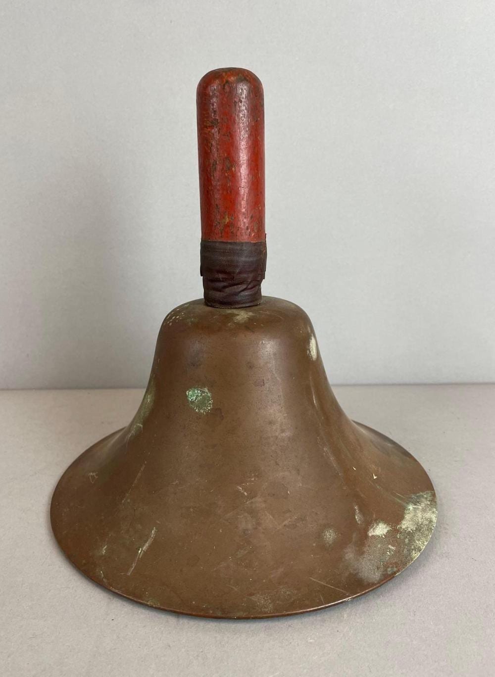 Vintage brass school bell with a flared dome and dark leather strap around the top.