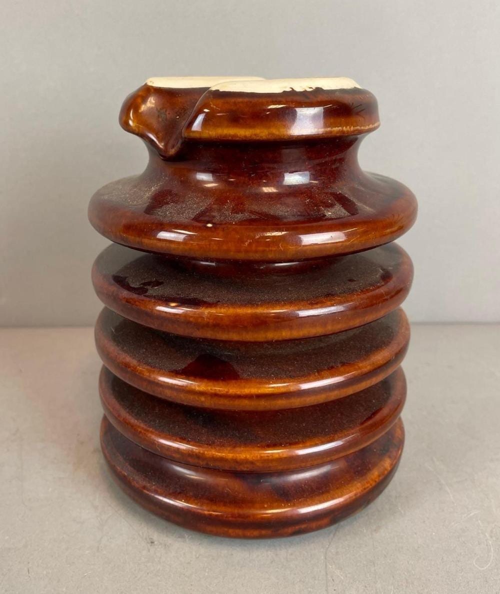 Brown ceramic insulator with a fluted, barrel-shaped body and flared top, photographed on a light background.