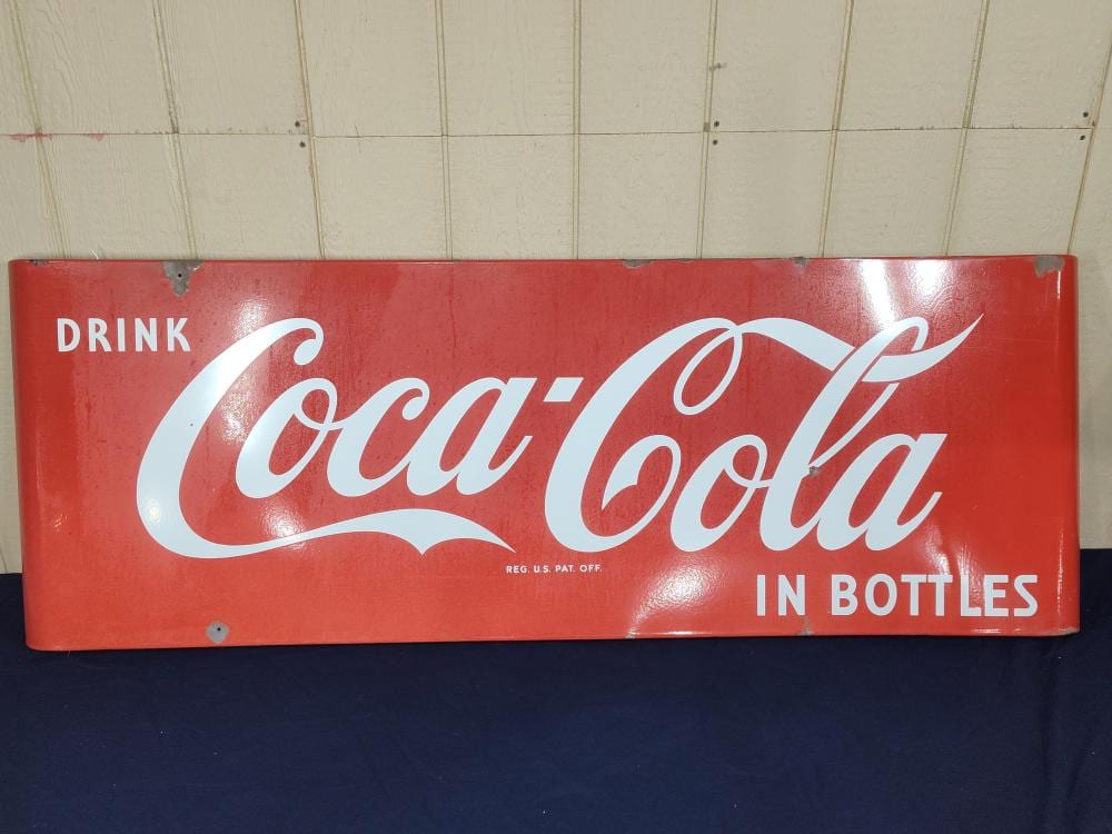 Red Coca-Cola sled sign with white script reading “Drink Coca-Cola in bottles.”
