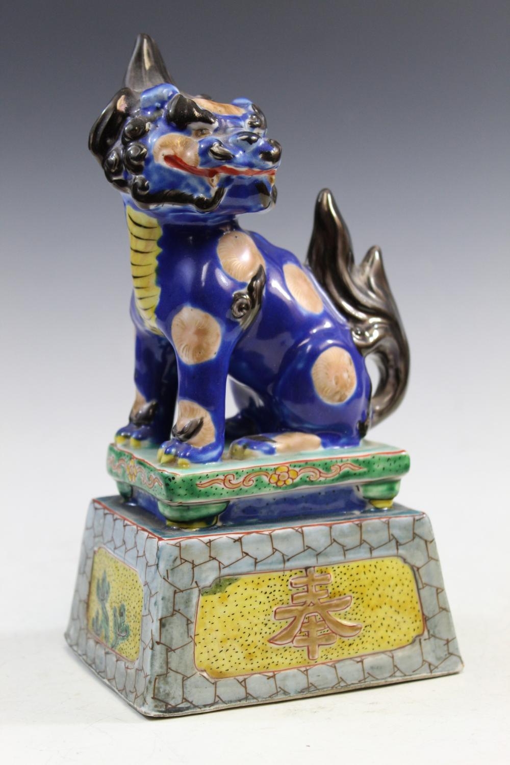Blue and white Chinese-style foo dog porcelain statue with a raised paw, seated on a decorated base with Chinese characters.