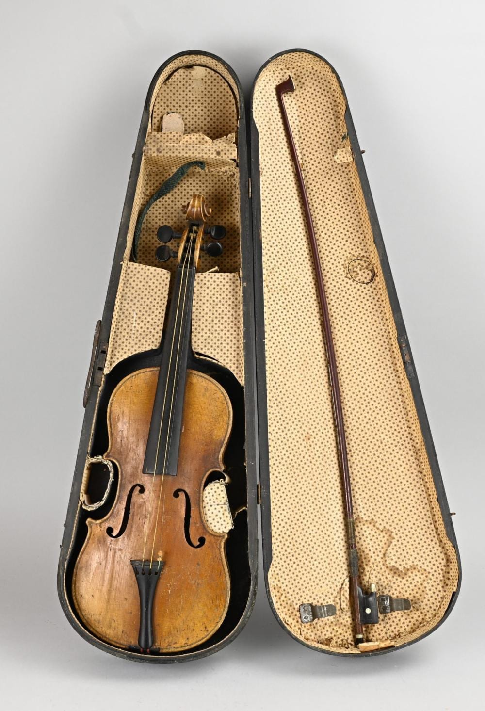 Front view of a brown violin with black chinrest and bridge, shown resting inside a beige speckled case.