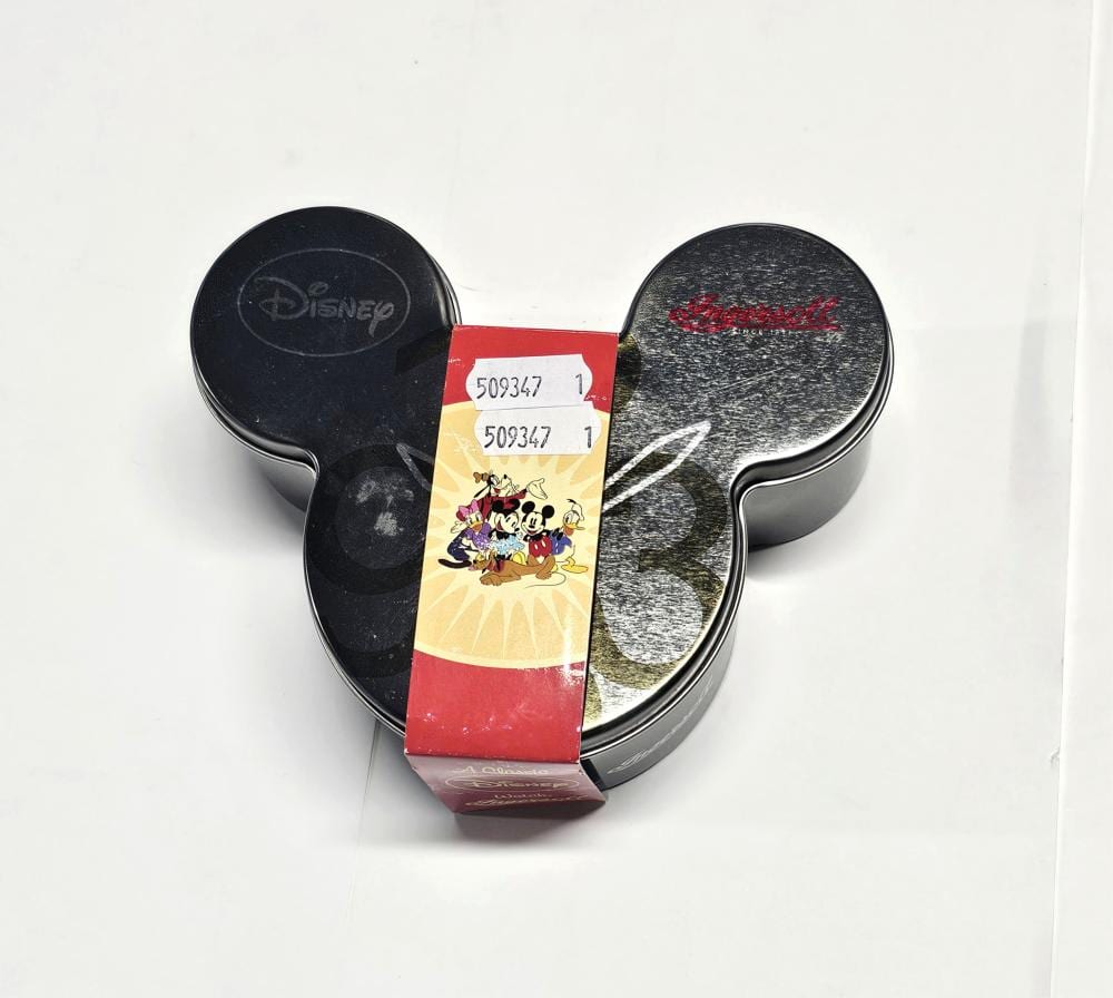 A Mickey Mouse–shaped tin/watch case with two round end panels (black and gray) and a paper label in the center.
