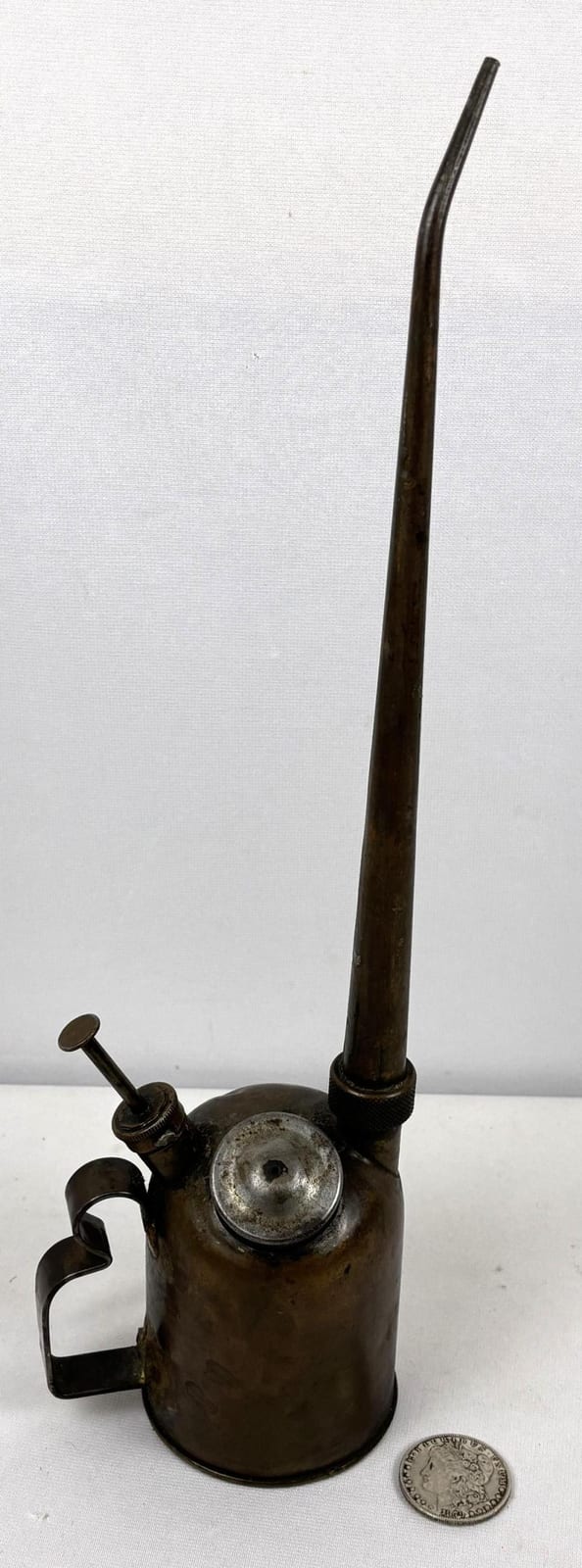 Small vintage metal oil can with long spout and pump handle, shown on a white background next to a coin for scale.