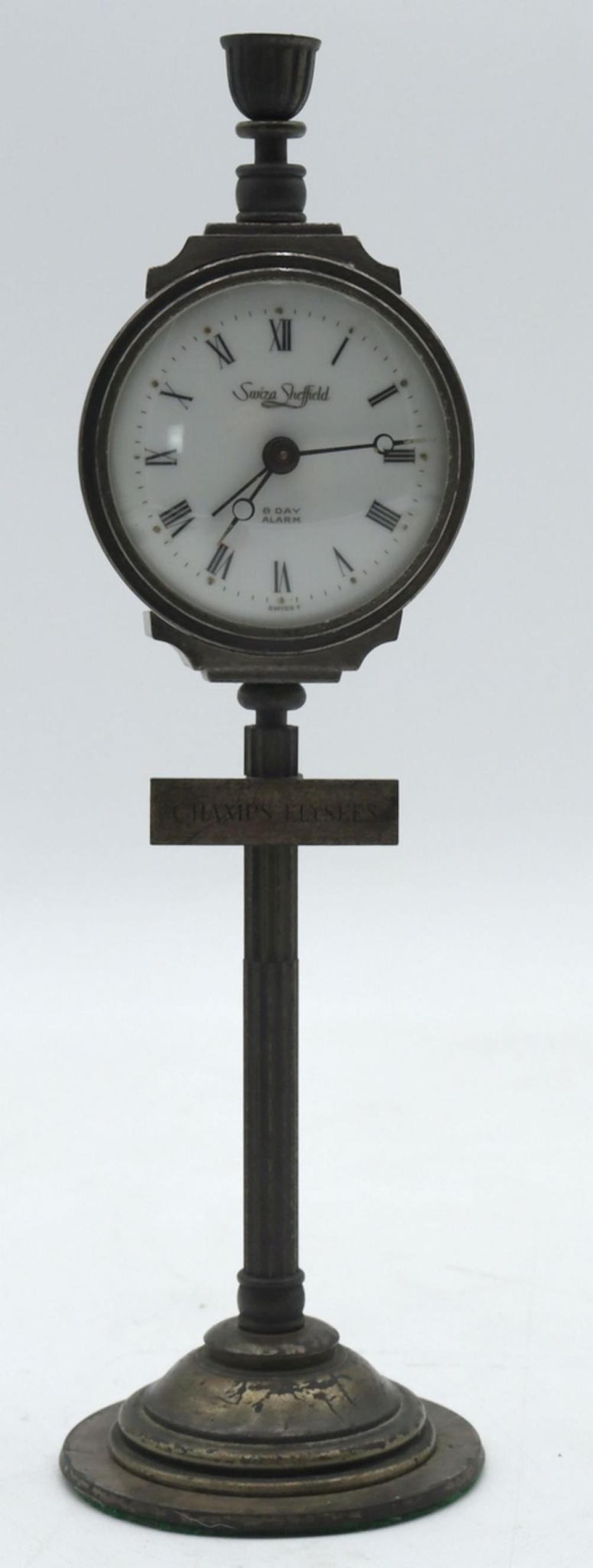 Black metal desk alarm clock with Roman numeral face and hands, showing the text “8 day alarm”.