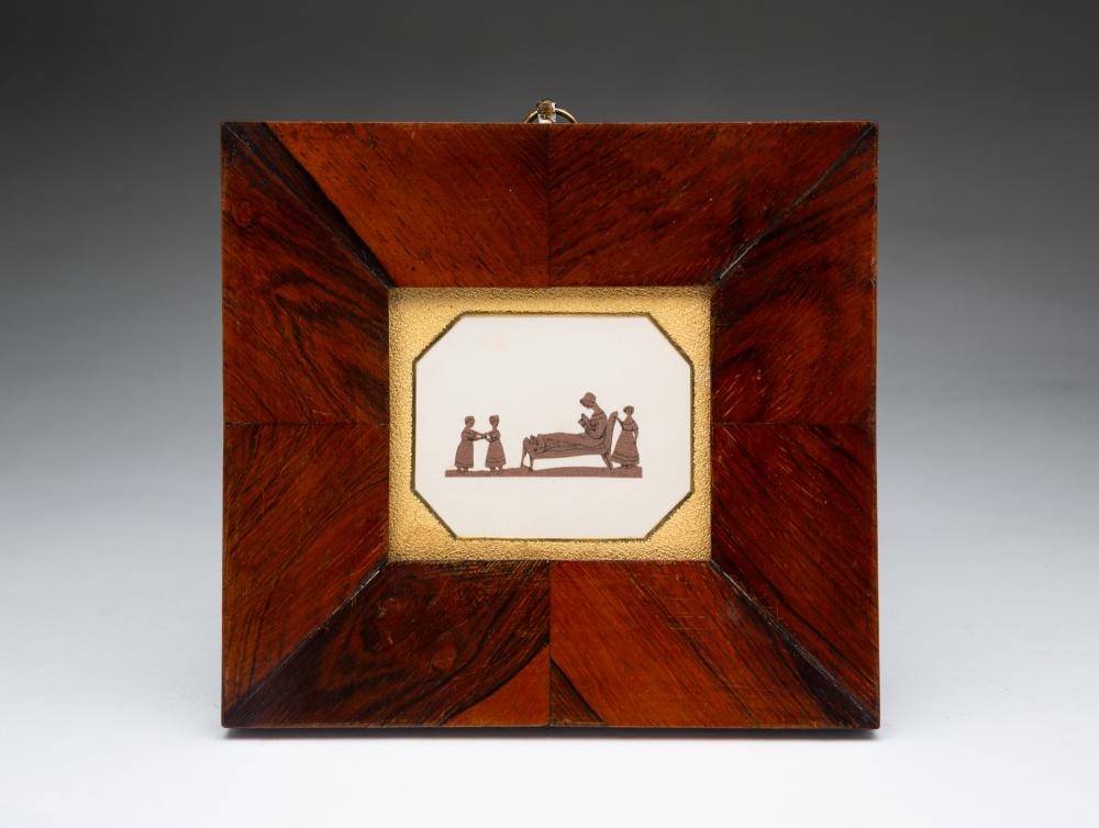 Closed miniature picture frame or box with an octagonal window showing cut paper and ink figures of people conversing and seated at a table.