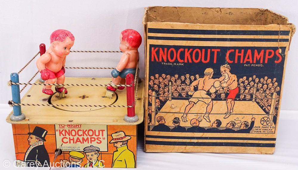Vintage wind-up tin toy boxing ring with two small boxer figures and a lithographed box labeled “KNOCKOUT CHAMPS.”
