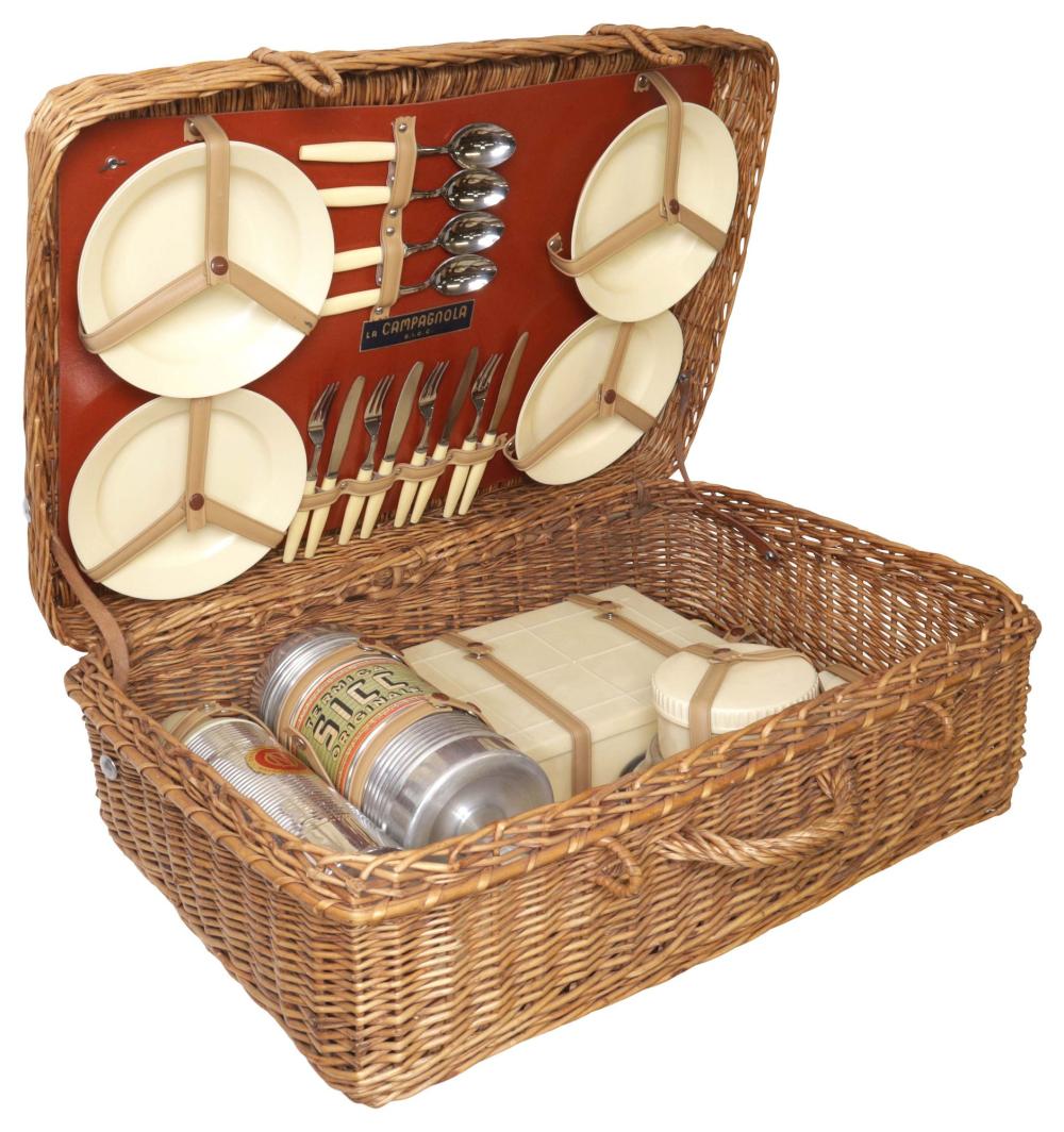Wicker picnic basket with split wood serving trays, metal cutlery, and condiment cans in the open compartment.
