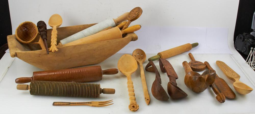 Assorted wooden kitchen utensils arranged on a table, including scoops, spatulas, a carved rolling pin, and a shallow bowl-shaped tool.