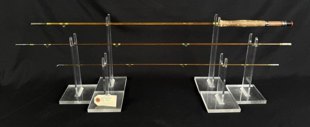 Photograph of two fly fishing rods displayed horizontally on clear acrylic stands over a dark background.