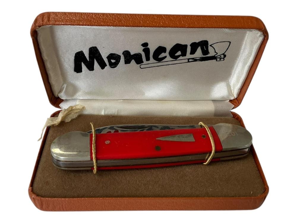 Red-and-silver pocket knife with a clip and two blades, resting in an open brown case with a white logo insert.