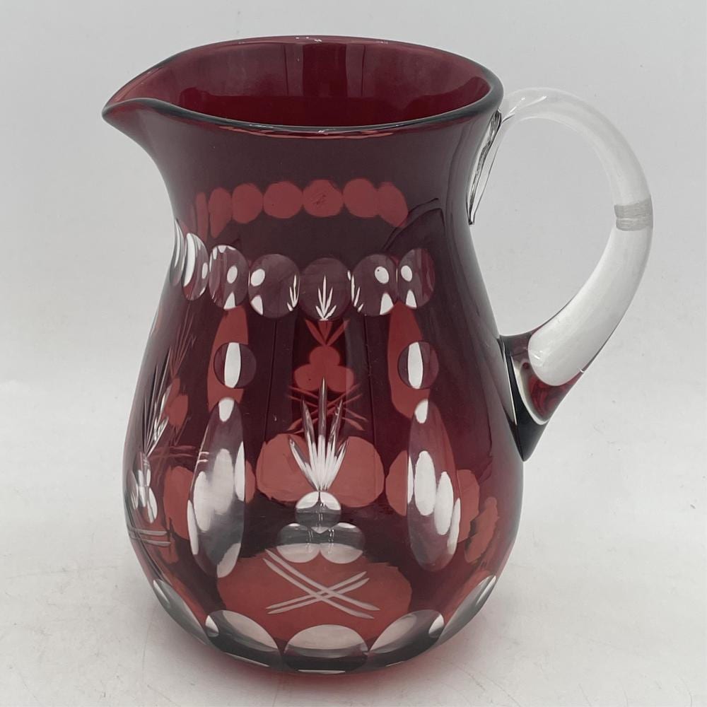 Ruby red cut glass pitcher with a clear handle and white floral and geometric motifs on the body.