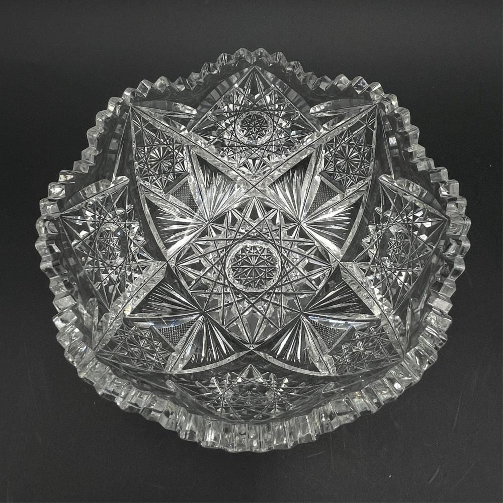 Clear cut-glass decorative bowl with star and diamond patterns and faceted rim, shown against a dark background.