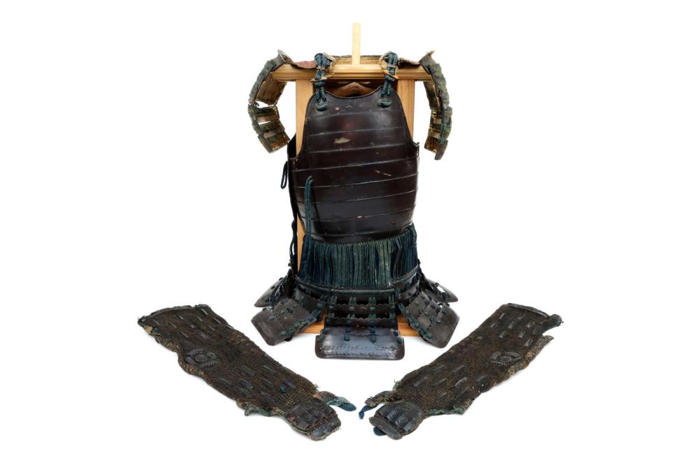 Front view of a dark Japanese samurai-style armor chest piece with layered arm guards and a blue-green waist sash, shown on a display stand.