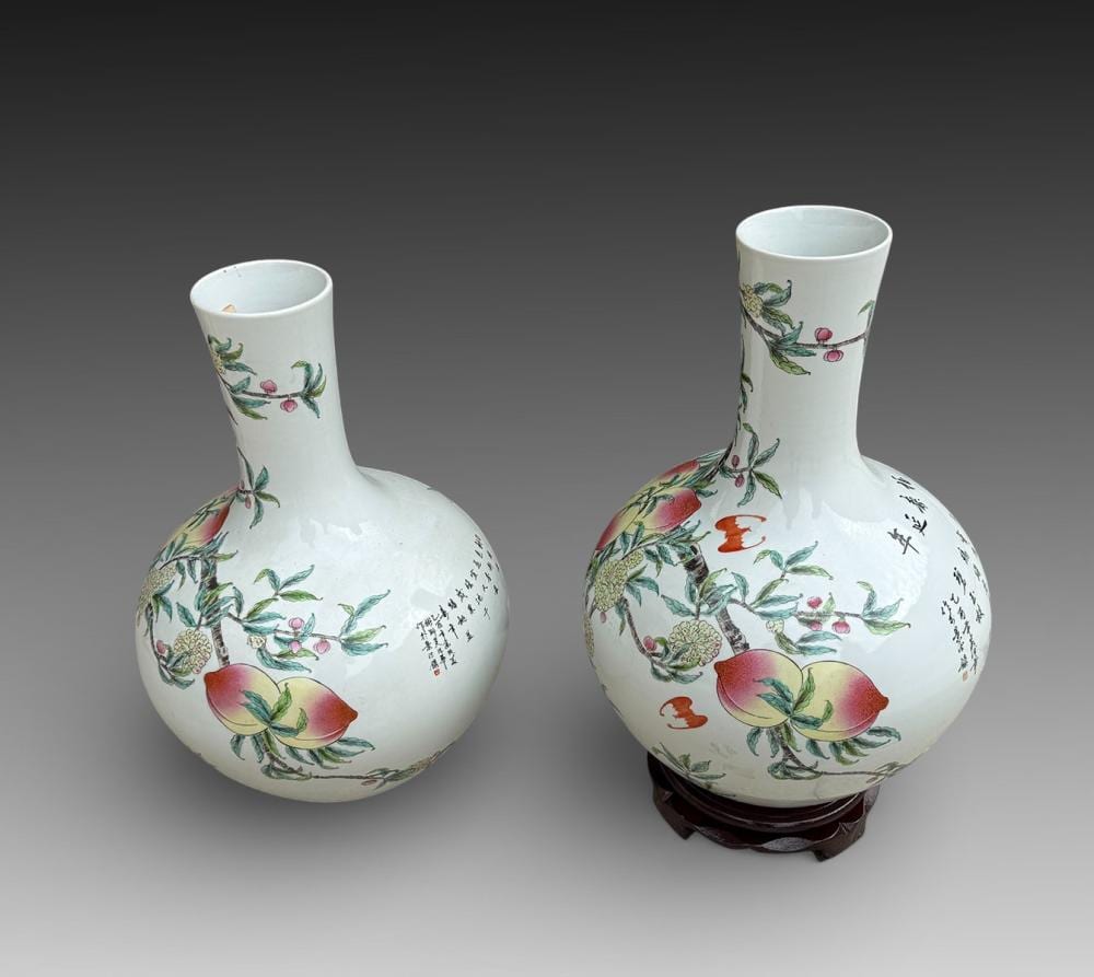 Pair of white porcelain vases with painted floral and fruit decoration in green, red, and pink, each with an upright neck and flared rim.