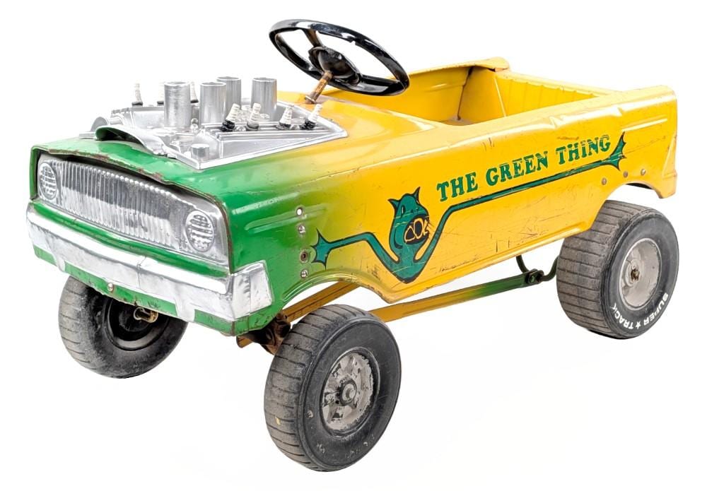Yellow and green toy pedal car with an open top and large wheels, decorated with “THE GREEN THING” on the side.
