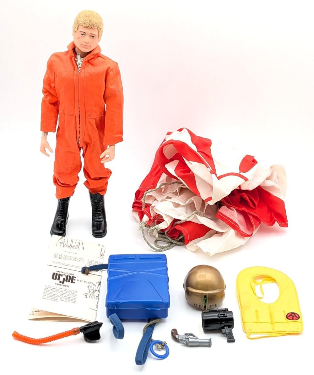 Vintage action pilot figure in a red flight suit and boots, with accessories including a blue case, parachute, helmet, and small weapons and straps.