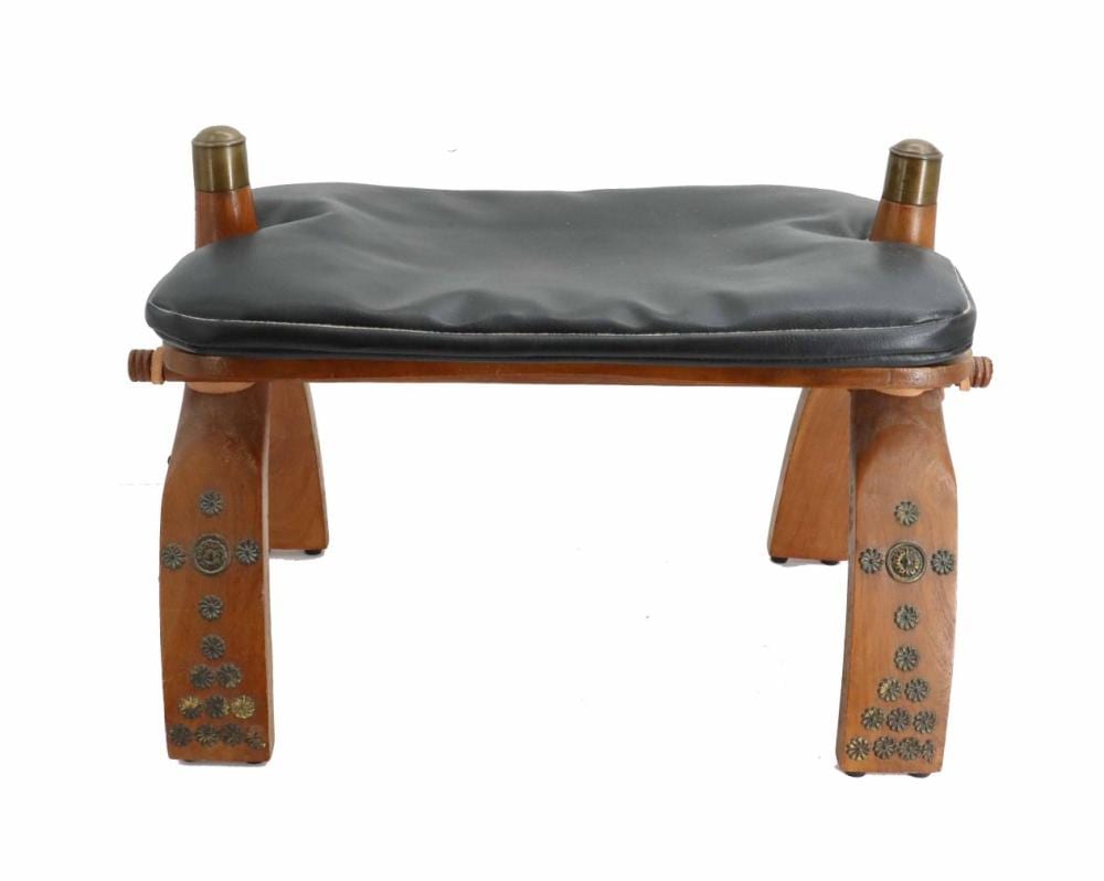 Brown wooden stool with carved decorative panels, two brass-colored posts at the top corners, and a padded dark seat cushion.