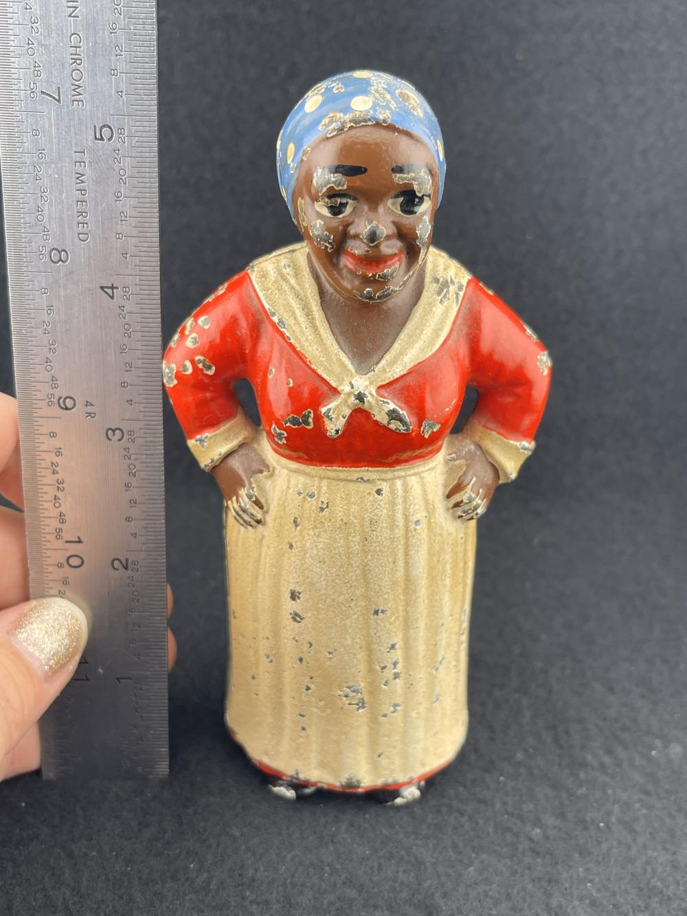 Small cast-iron piggy bank shaped like a boy in a red robe and gold tunic with a blue cap, shown against a dark background.