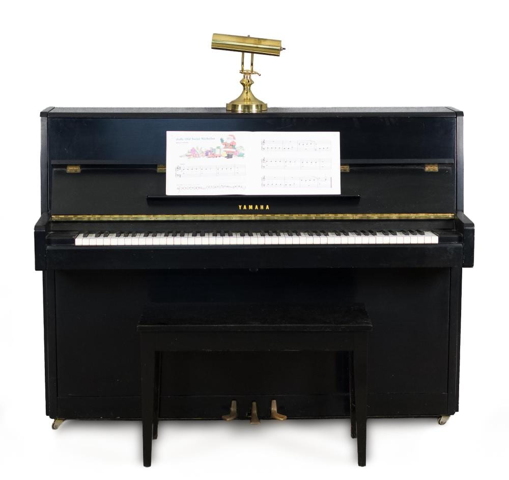 Black upright Yamaha piano with gold trim, music sheet on the stand, and a small gold bell-shaped ornament on top.