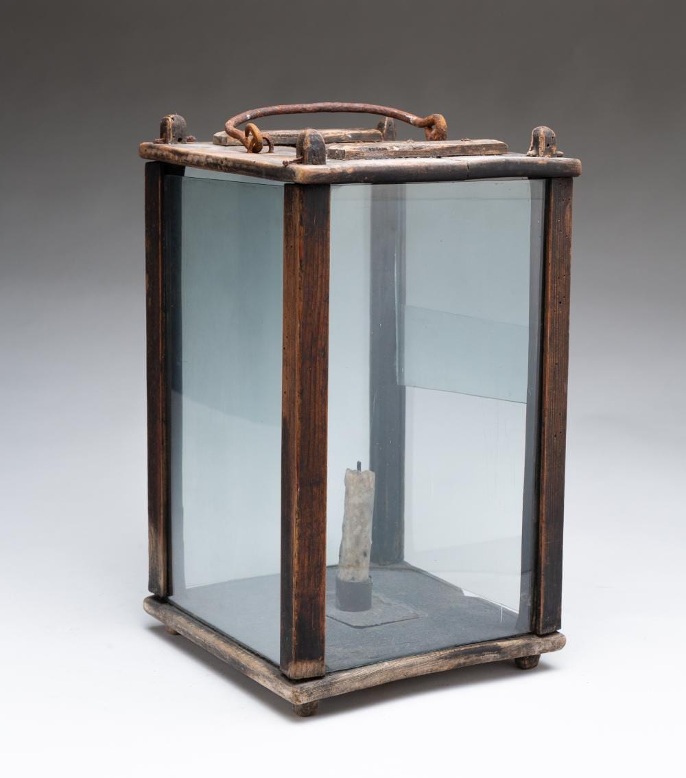 Rectangular wooden barn-style lantern with a glass panel enclosure and metal handle on top, photographed against a gray background.