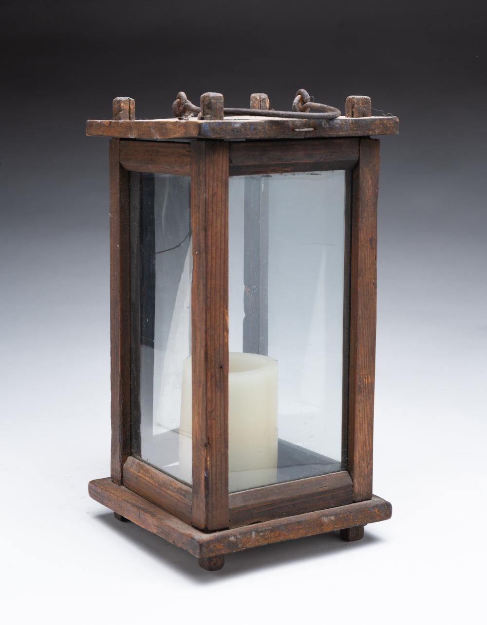 Rustic wooden barn lantern with clear glass panels and a metal handle on top, with a white candle inside.