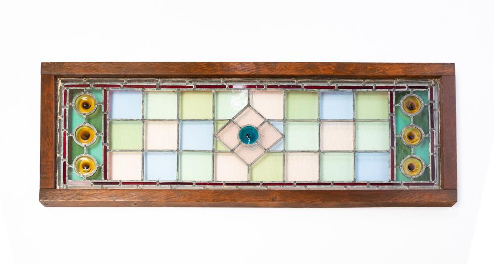 Wood framed leaded stained glass window panel with green, blue, and white geometric grid and circular accents at the sides.