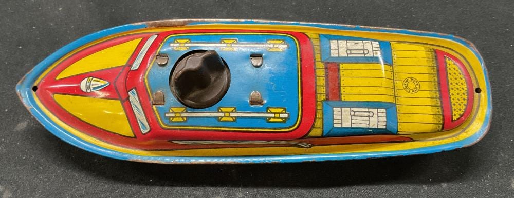 Top view of a colorful wind-up toy boat with a blue stripe, yellow and red graphics, and a black crank housing.