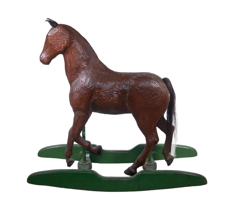 Brown carved wooden rocking horse figurine with a green base, shown from the side against a white background.