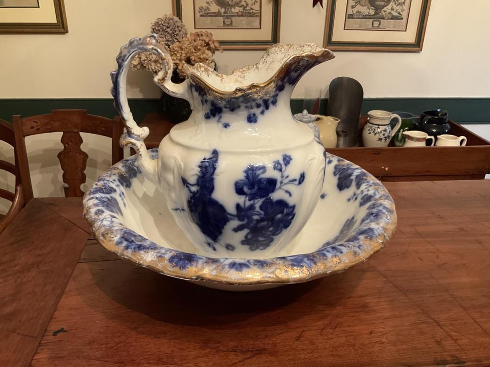 White and blue flowery ceramic pitcher and matching wash basin set, with floral transfer-print decoration and cracked blue glaze around the basin rim.