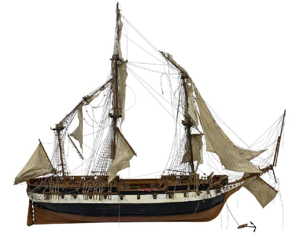 Wooden model sailing ship with multiple masts, rigging lines, and tan sails displayed on a white background.