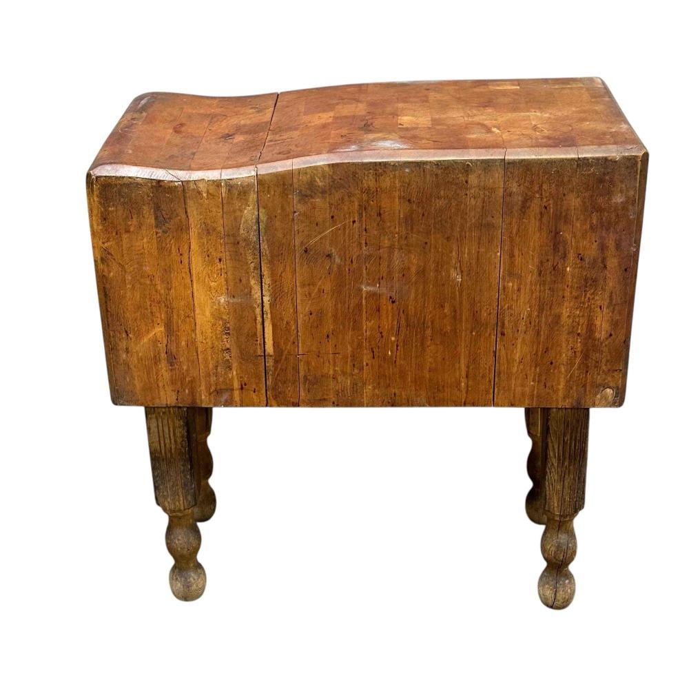 Antique wooden butcher block table with paneled body and turned legs, shown from the front on a white background.