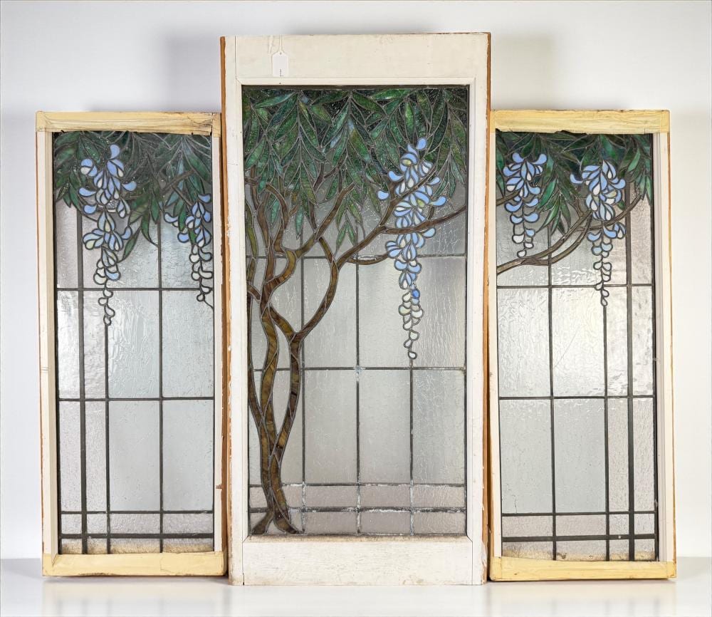 Three-panel stained-glass window with green vine and blue grape cluster designs set in dark metal leading, on a light frame.