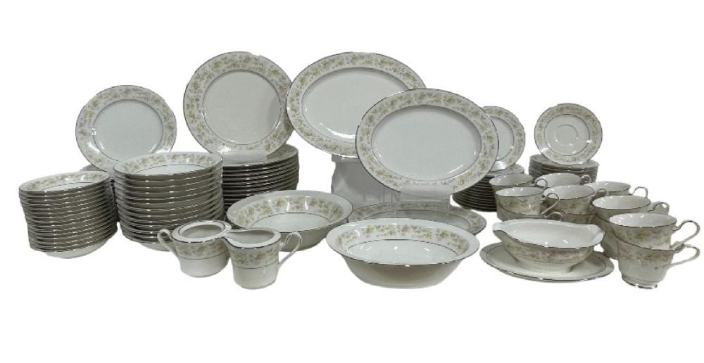 White porcelain dinnerware set arranged in stacks with floral-patterned rims, including plates, bowls, and teacups with saucers.