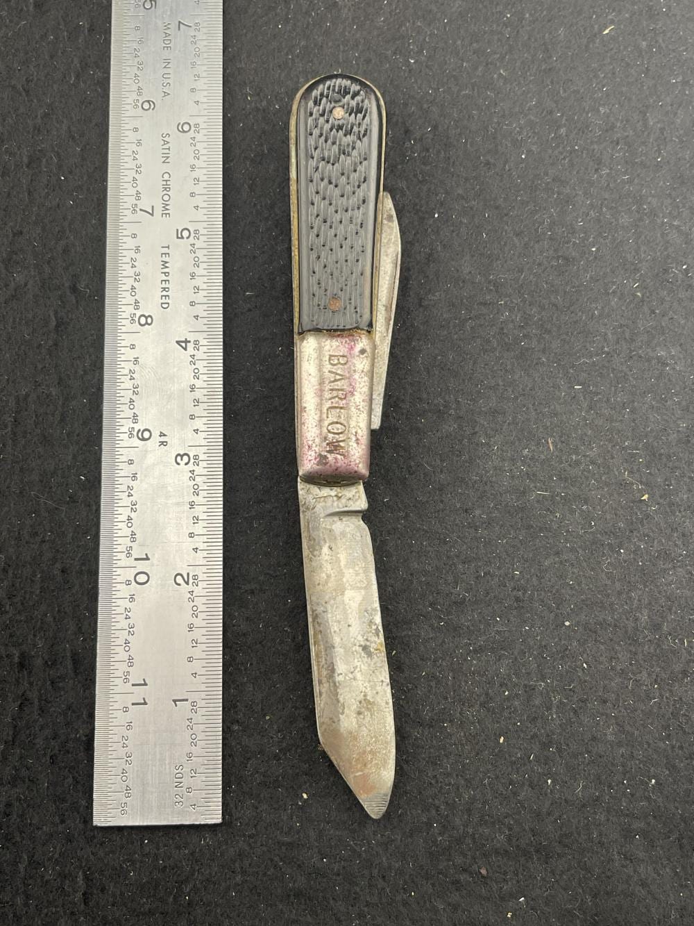 Open pocket knife with a stainless steel blade and a ribbed handle featuring a pink decorative panel, shown on a black surface.