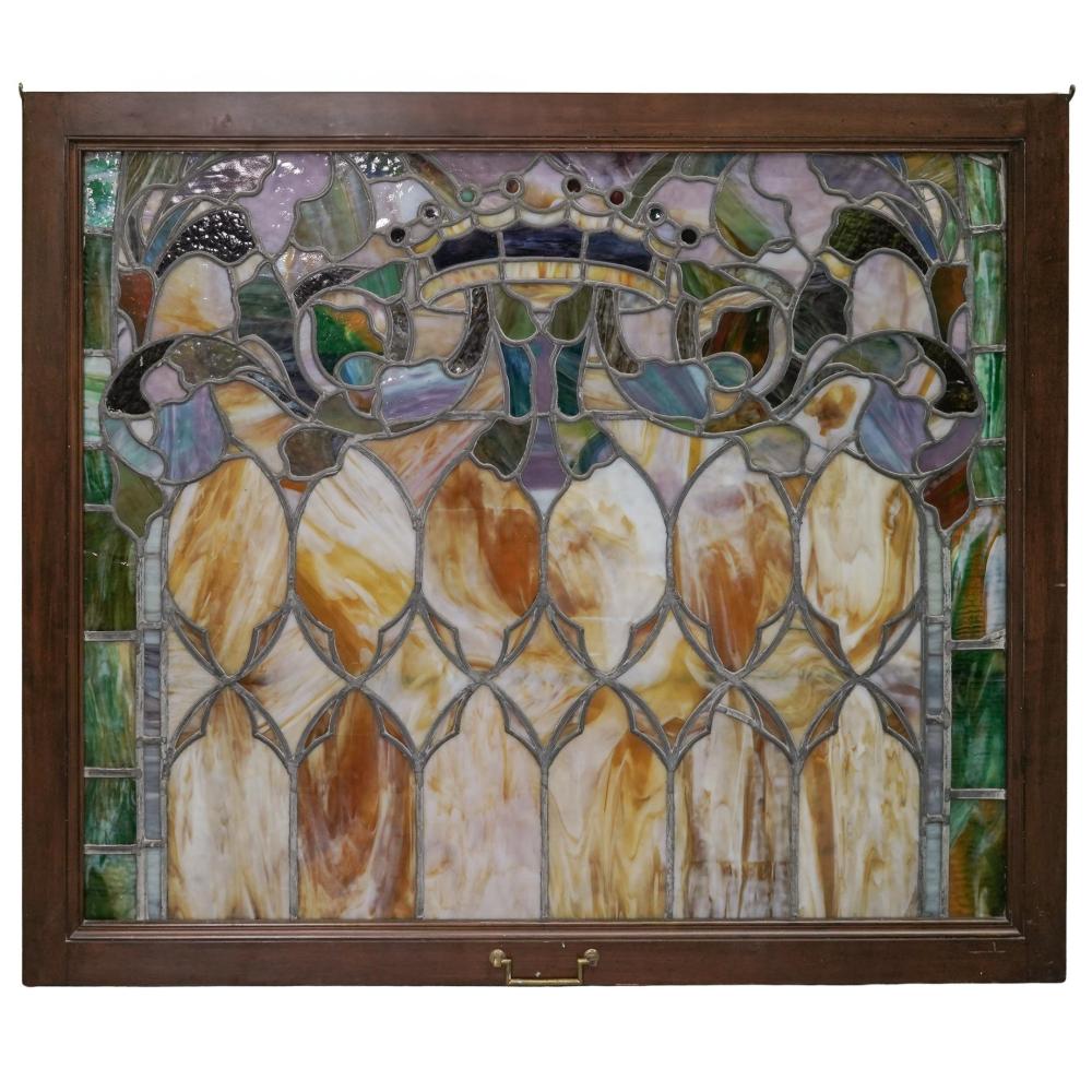 Stained glass window panel with arched leaf-like shapes and multicolored amber, white, and green glass set in a dark frame.